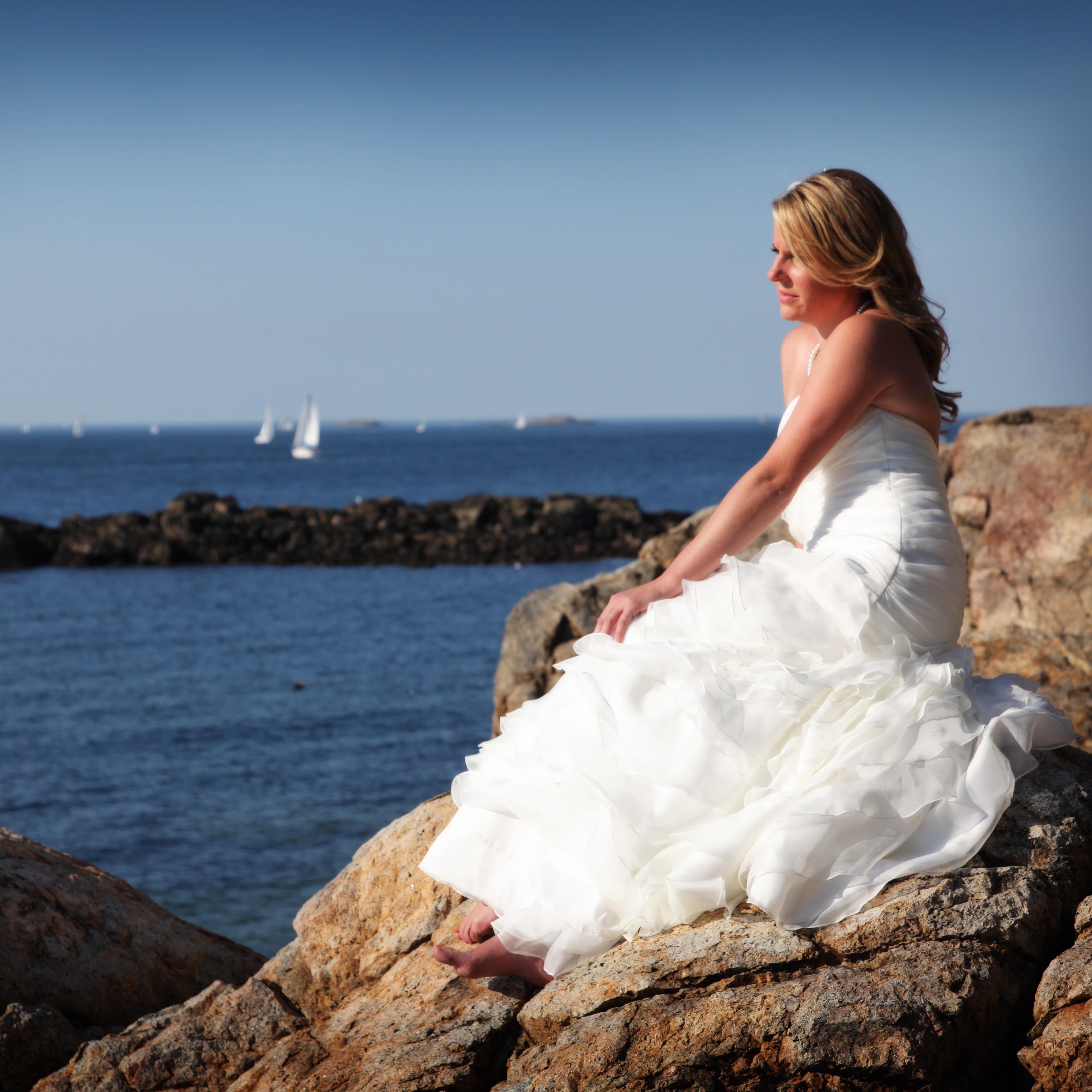 bride sitting in wedding dress on rocks overlooking the ocean
